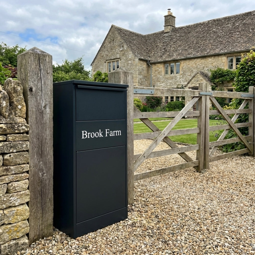 Black mailbox with 'Brook Farm' branding in front of a stone building and wooden gate.  GLOPBX103RABLK